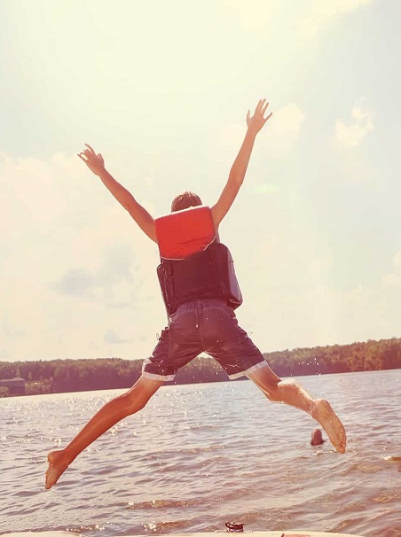 Man wearing a lifejacket jumping into a lake